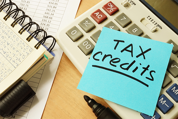 Tax Credit text written on sticky note next to calculator and financial worksheets