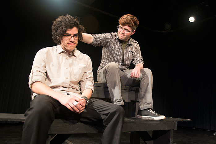 Two male actors sitting down, one has his hand on the other actor's head