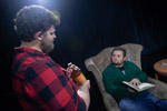 Theater student in red flannel standing next to student in green sweater sitting in a chair