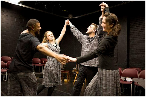 4 actors wearing black and grey holding hands in a circle