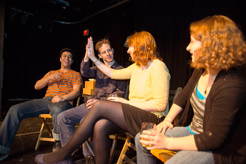 4 actors sitting in chairs, two are giving each other a high five