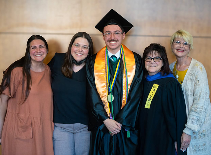 Graduate in cap and gown poses with four supporters after commencement, smiling for a group photo.