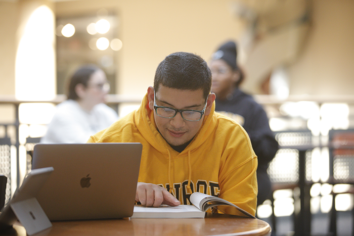 Student at a desk studying a book with a laptop nearby