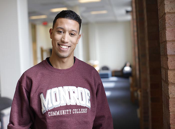 a student in a maroon "monroe community college" sweatshirt smiling