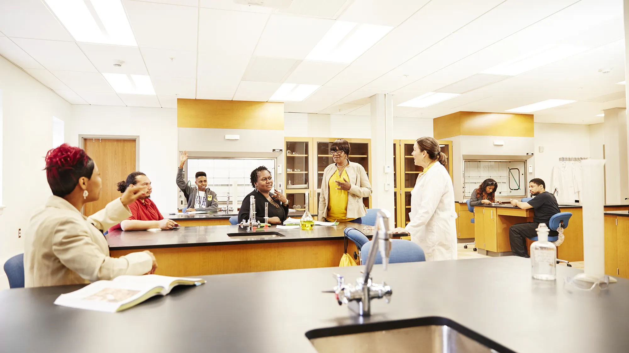 A professor speaks with students in a lab classroom