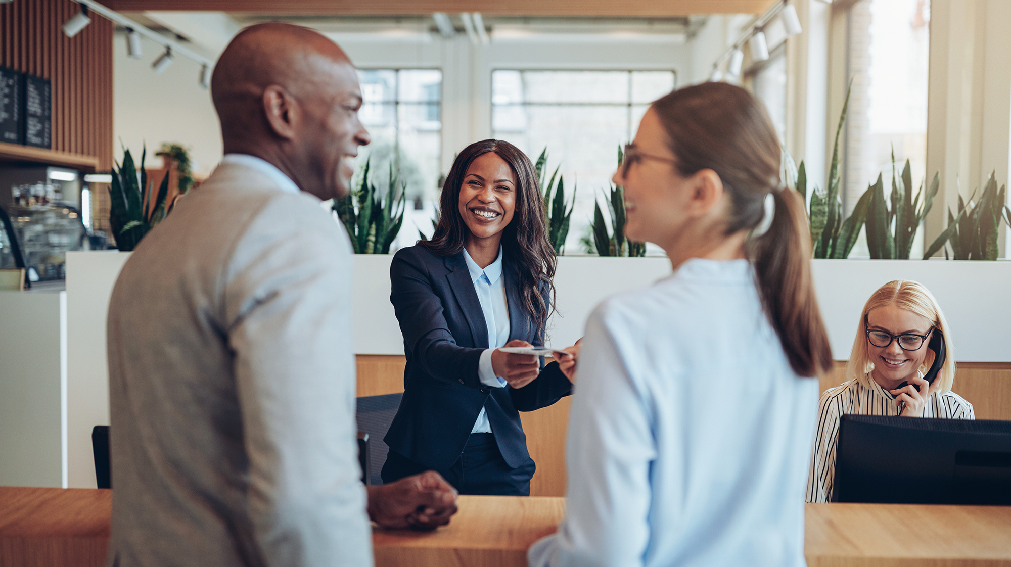 Woman at a front desk helping two people check into a hotel, they are all smiling at each other.