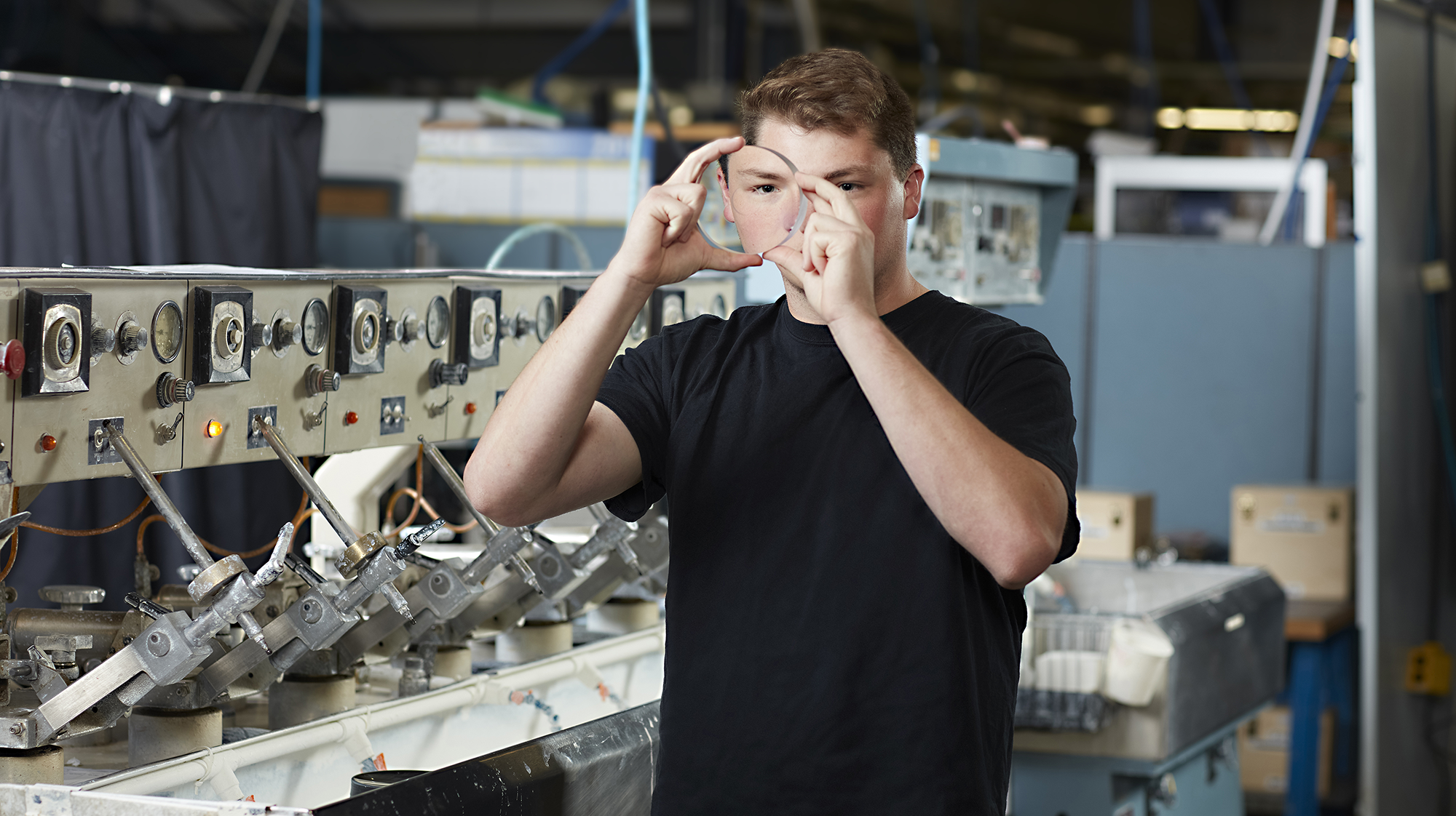 Student inspects an optical lens while working with manufacturing equipment in an optics laboratory.