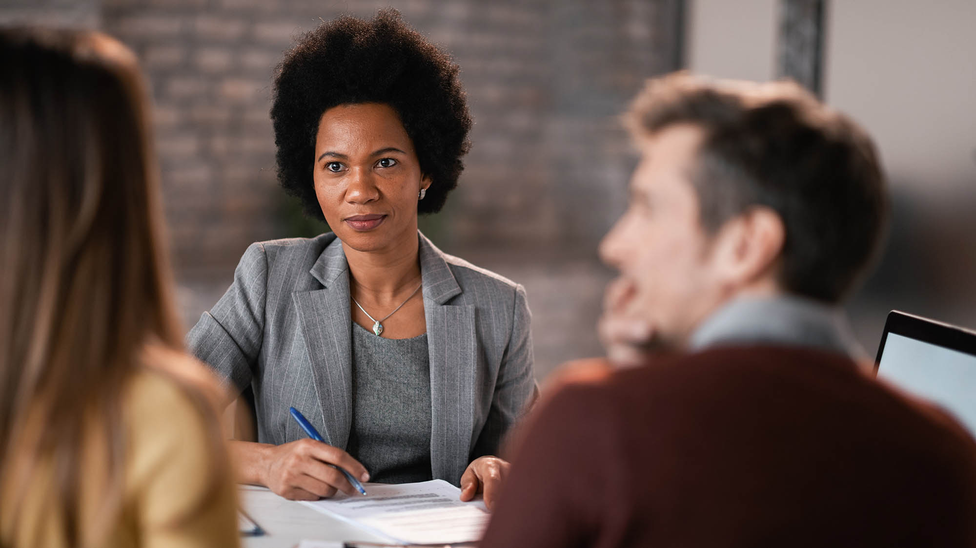 A professional meeting with a woman reviewing documents with two colleagues at a table.