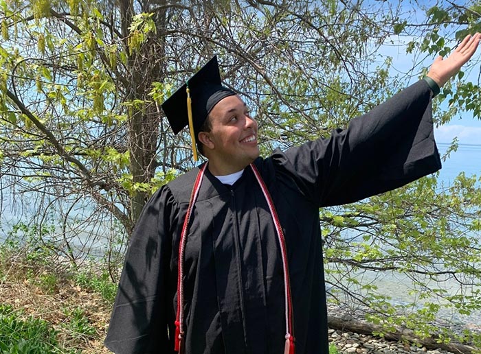 a student in a graduation cap and gown gesturing to the right