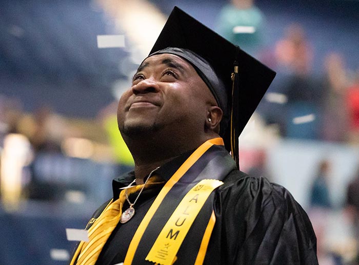an alumni smiling in graduation attire with confetti surrounding them