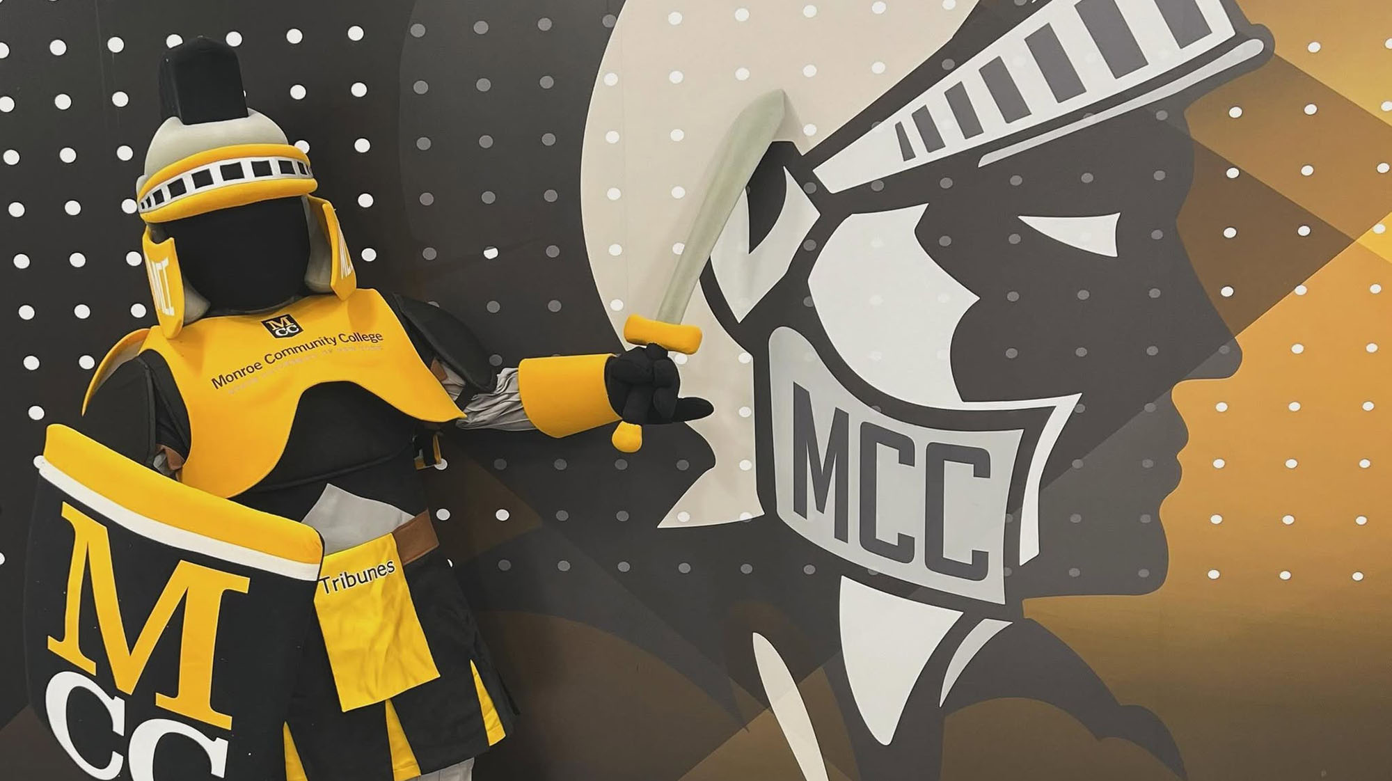 Tiberius the Tribune, the MCC mascot, posing with a tribune head logo with "MCC" on it